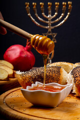 Honey dripping from a spoon on a table in Rosh Hashanah next to an apple, pomegranate and challah...