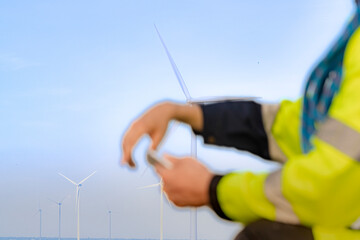Workers in high visibility jackets examine a wind turbine farm, one pointing towards the turbines...
