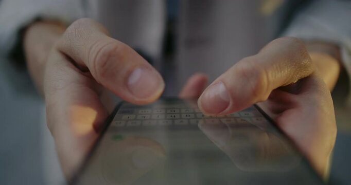 Camera view from top of smartphone screen. Person typing message on touch screen with both thumbs. On display visible message entering and keyboard at bottom. Remote communication.