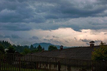 old roof elongated with many chimneys and dark cloudy sky on the background of the mountains
