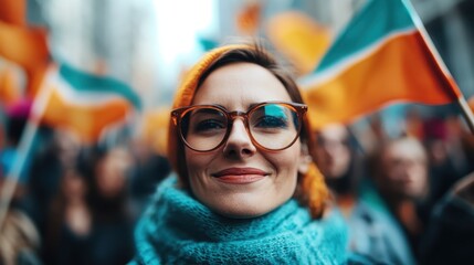 A joyful woman wearing glasses stands amidst a crowd, proudly holding Irish flags, radiating happiness and national pride during a lively public event.