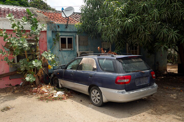 Fototapeta premium Colorful old building in colonial style and junked car in narrow street with palm trees in Oranjestad in Aruba during spring time.