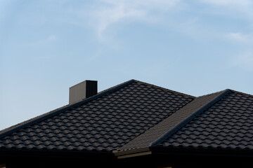 The rooftops of a cozy house rise against a bright blue sky, showcasing intricate tiles and a prominent chimney, inviting a sense of warmth and tranquility