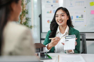 Smiling real estate agent holding a calculator is discussing house prices with her client