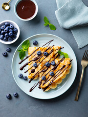 Crepes, thin pancakes with chocolate sauce and fresh blueberries. Grey background. Top view.