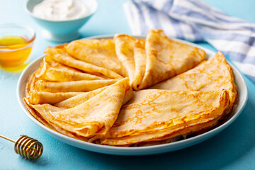 Crepes, thin pancakes on a plate with honey and cream. Blue background. Close up.