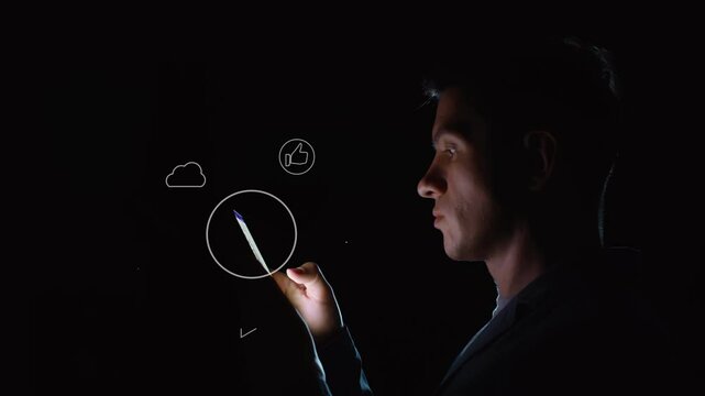 A young adult uses a smartphone in complete darkness, only the face and monitor are illuminated. Symbols with thematic content being viewed rotate around the screen. Cg