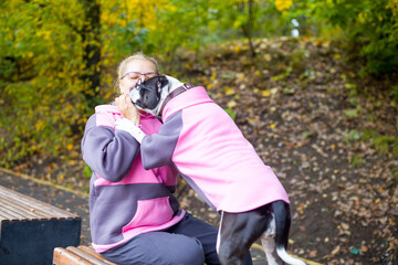an adult woman in a tracksuit on a walk with a dog. A dog in a fashionable sweater and glasses