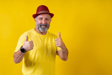 A man in a yellow shirt is wearing a red hat and giving a thumbs up