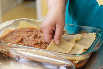 Chef is carefully layering lasagna noodles over meat sauce, showcasing the meticulous process of preparing this classic italian dish. Selective focus