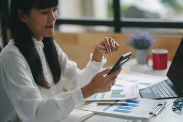 Focused businesswoman calculating expenses in office surrounded by paperwork, laptop, smartphone,...
