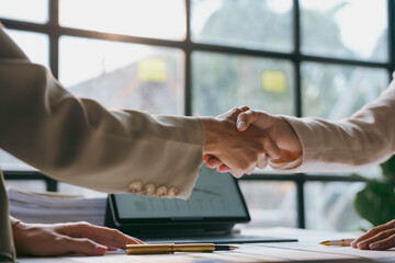 Two businesswomen are shaking hands after reaching an agreement during a business meeting