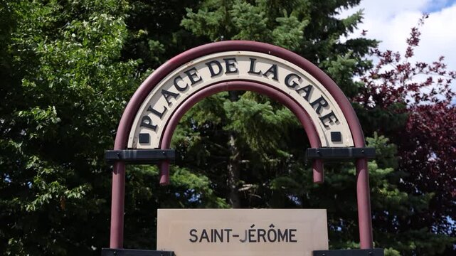 Slow motion wind blowing through trees behind place de la gare sign in saint jerome quebec canada. Selective focus