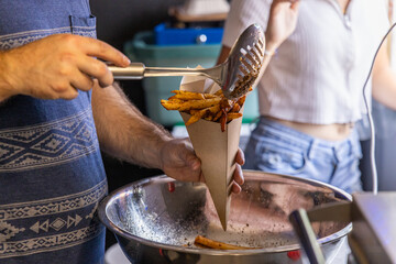 Street food vendor is adding seasoning to an order of french fries for a customer. Selective focus