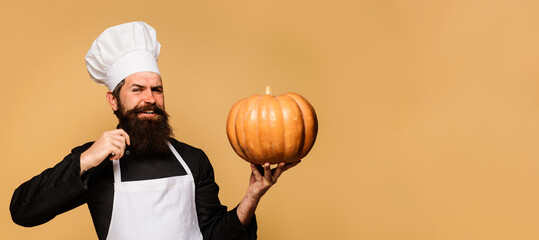 Fototapeta premium Smiling male cook in chef hat with big pumpkin. Autumn recipes. Healthy vegetarian eating. Bearded man in chef uniform with pumpkin for Halloween. Thanksgiving day cooking. Copy space for advertising.