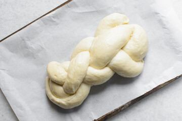 Overhead view of proofed challah dough on a parchment lined baking sheet, top view of braided challah loaf on a baking tray