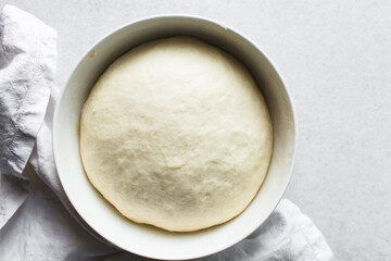 Overhead view of proofed challah dough in a white mixing bowl, top view of homemade challah dough rising in a white mixing bowl, process of making challah