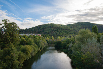 View of the Sil River as it passes through the city of Ponferrada under a pedestrian bridge and a railway bridge that gives access to the train station and the Pajariel mountain in the background