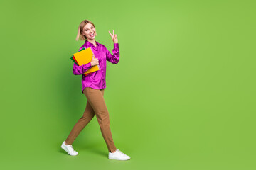 Full size photo of pretty young woman book walk empty space v-sign wear shirt isolated on green color background