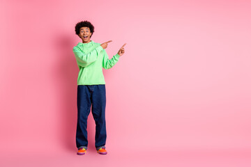 Full size photo of nice young man direct fingers empty space wear green hoodie isolated on pink...