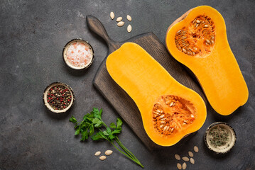 Halves of raw butternut pumpkin with spices on a wooden cutting board, dark grunge background, top view, flat lay, copy space