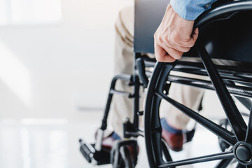 Close-up of disabled senior man sitting in wheelchair and moving indoors