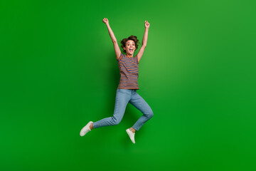 Full length portrait of delighted carefree person jumping raise fists achievement empty space isolated on green color background