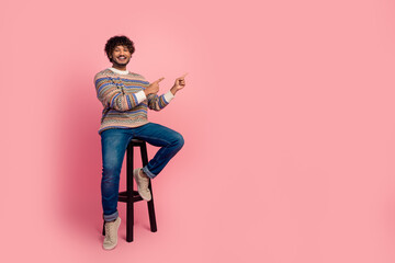 Full body photo of nice young man sit stool point fingers empty space isolated on pink color...