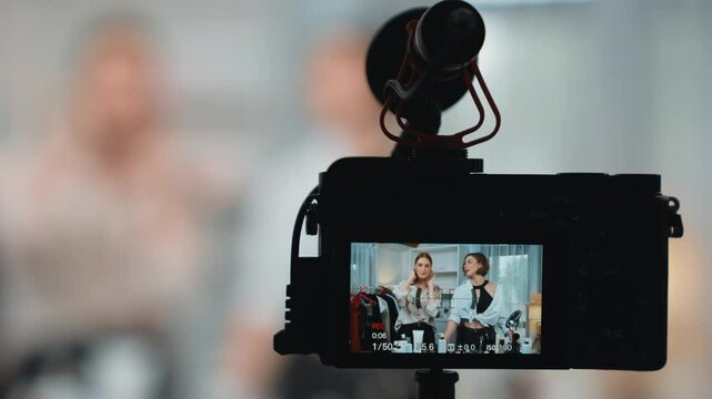 Rear view behide camera screen display two women influencer shoot vlog video review clothes prim social media or blog. Girls with apparel studio lighting for live streaming marketing recording session