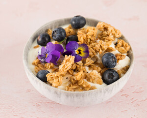 A healthy nutritious breakfast of natural Greek yoghurts, granola and fresh berries on pink background.