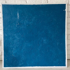 Textured deep blue panel is set against a white brick wall, emphasizing its rich color and intricate surface patterns. This composition reflects a perfect blend of modern art and minimalistic design