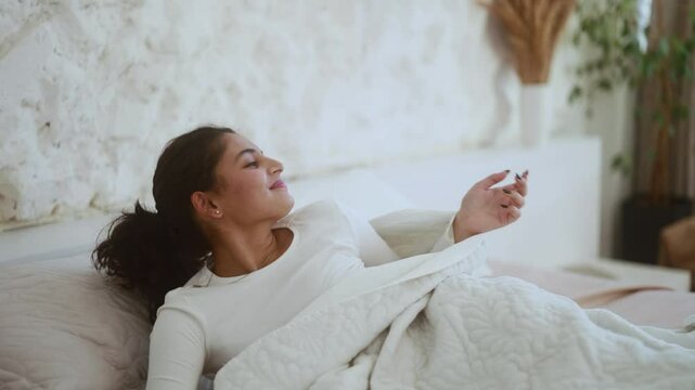 Happy sleepy young indian woman waking up lying in bed at light room Pretty female stretching enjoying early good morning before study or work in cozy bedroom Beautiful morning and good day