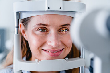 Close up front view photo of young smiling female patient undergoing sight ophthalmic check up