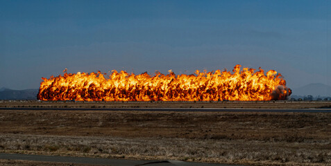 A dramatic image of a row of fire created by a munitions explosion with against a blue sky