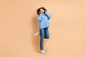 Fototapeta premium Photo of young beautiful woman in stylish clothes enjoy listen music blue bluetooth headphones chilling isolated on beige color background
