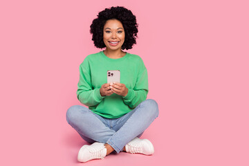 Full length photo of charming positive woman wear green sweatshirt texting sms modern gadget empty space isolated pink color background