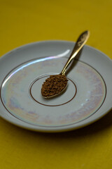 A spoon filled with coffee lies on a saucer on a yellow background. Coffee time