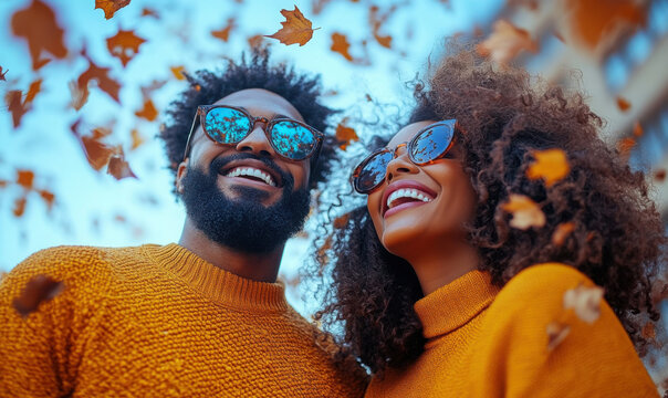 Afro couple throwing autumn leaves, walking in a park, and having fun
