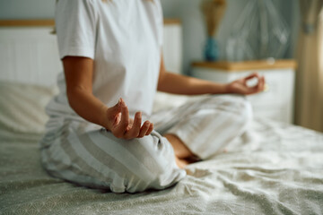 Close up of woman in lotus pose doing Yoga in bedroom.