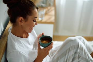 Happy woman enjoying in morning coffee in bedroom.