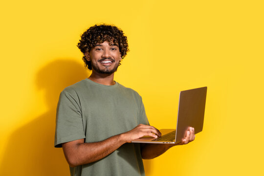 Photo of clever guy with wavy hairstyle dressed khaki t-shirt holding laptop in hands chatting isolated on yellow color background