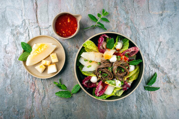 Mixed green leafy summer salad with Japanese soba buckwheat noodle, honeydew melon and peppermint served as top view with sweet sour chili dressing in a design plate