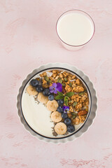 A healthy nutritious breakfast of natural Greek yoghurts, granola and fresh berries on pink background.
