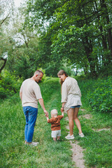 Obraz premium A family couple with a small son are standing in the park on the grass. Mother, father and child walk. Happy family with a child.