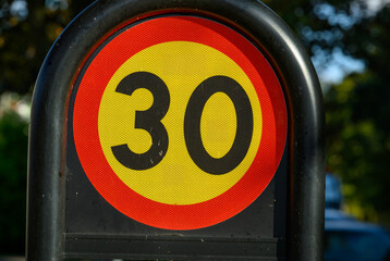 A circular speed limit sign displays a 30 kph limit, prominently situated in a residential neighborhood under clear, natural lighting
