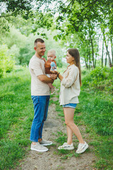 Fototapeta premium Mom, dad and little son on a walk in the park. Concept of parent time with child. Happy family couple with child in nature.