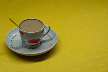 A golden spoon with coffee. Mug in a saucer on a yellow background. Coffee time