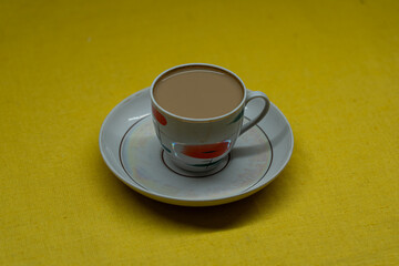 A mug of coffee with milk. Mug in a saucer on a yellow background. Top-down view