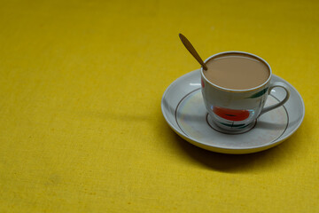 A golden spoon with coffee. Mug in a saucer on a yellow background. Coffee time