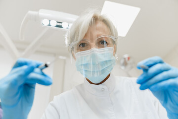 Low angle view of a caucasian middle-aged female dentist orthodontist stomatologist operating...